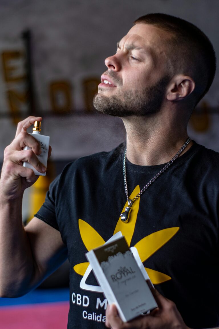 Man with short hair applying perfume while holding a box. Casual fashion and fragrance concept.