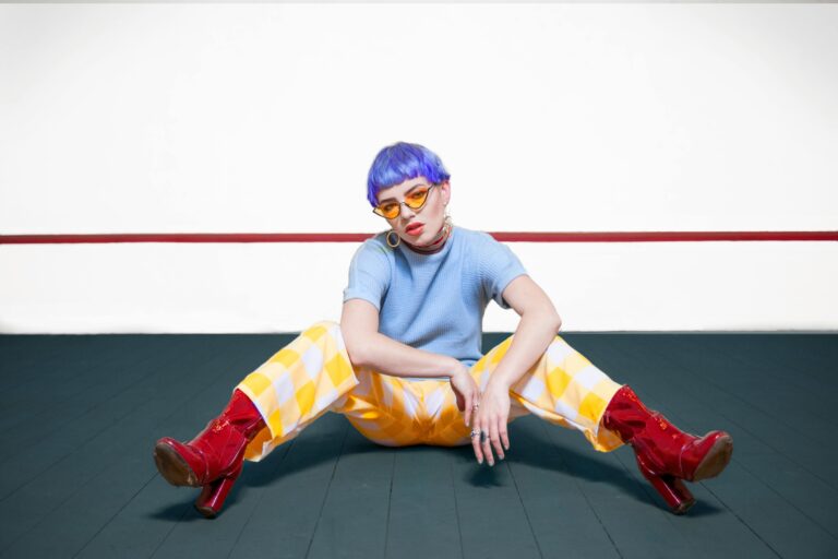 A fashionable woman with blue hair posing indoors in colorful attire, showcasing modern style.