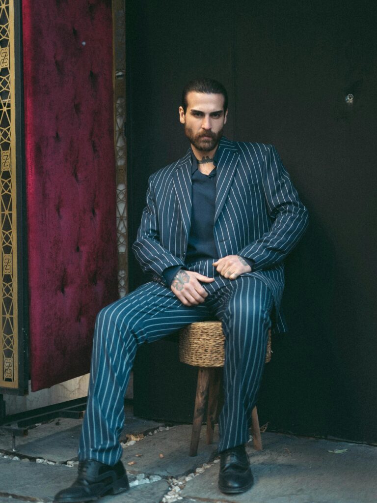 Fashionable man in a pinstripe suit seated outside a velvet-curtained entrance.
