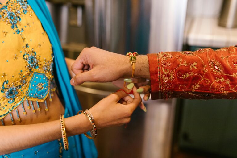 Close-up of a woman tying a rakhi on a man's wrist during a traditional Indian ceremony.