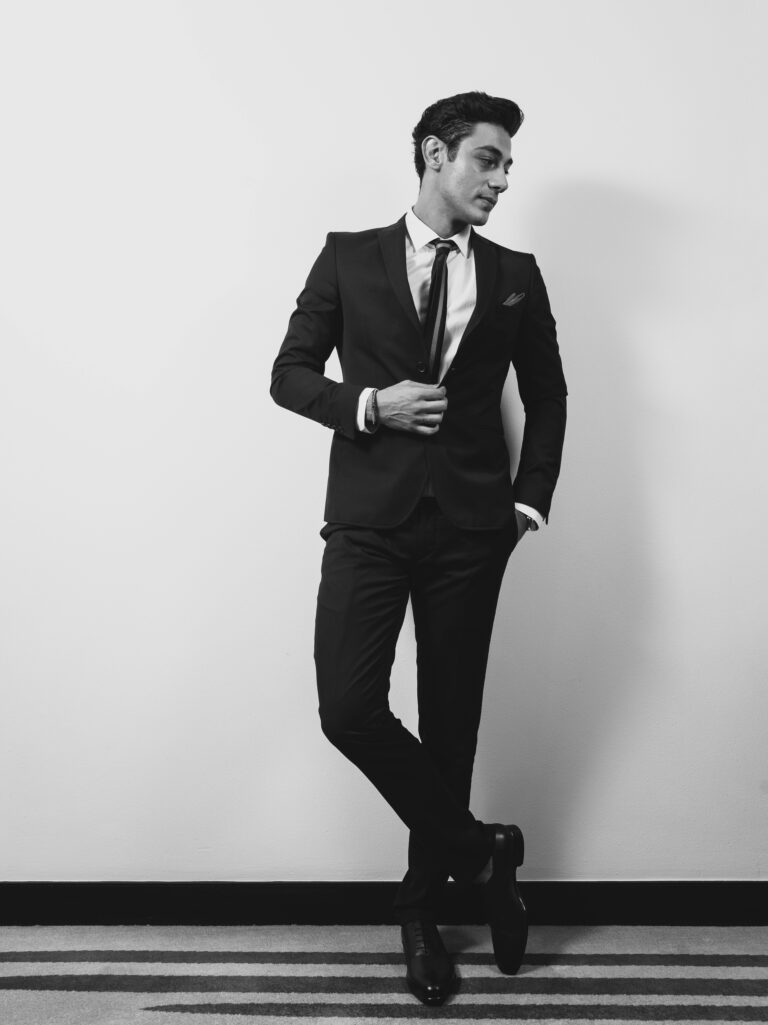 Black and white portrait of a sophisticated man in formal attire striking a confident pose.